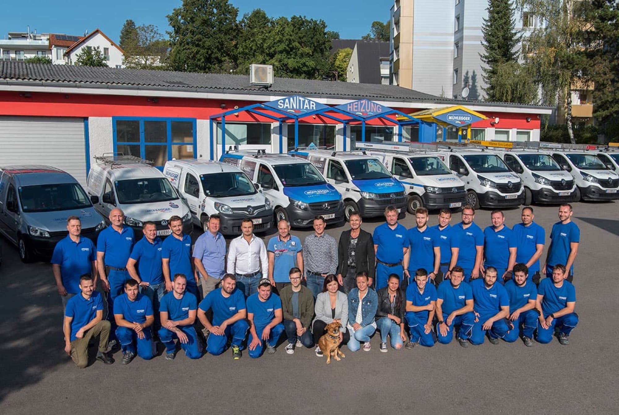 Team vor dem Firmengebäude mit Firmenfahrzeugen
